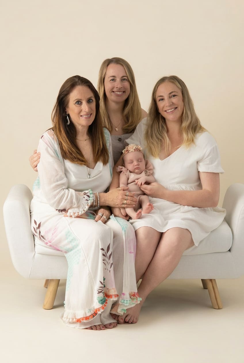 Parents leaning in to kiss their newborn son on a white backdrop