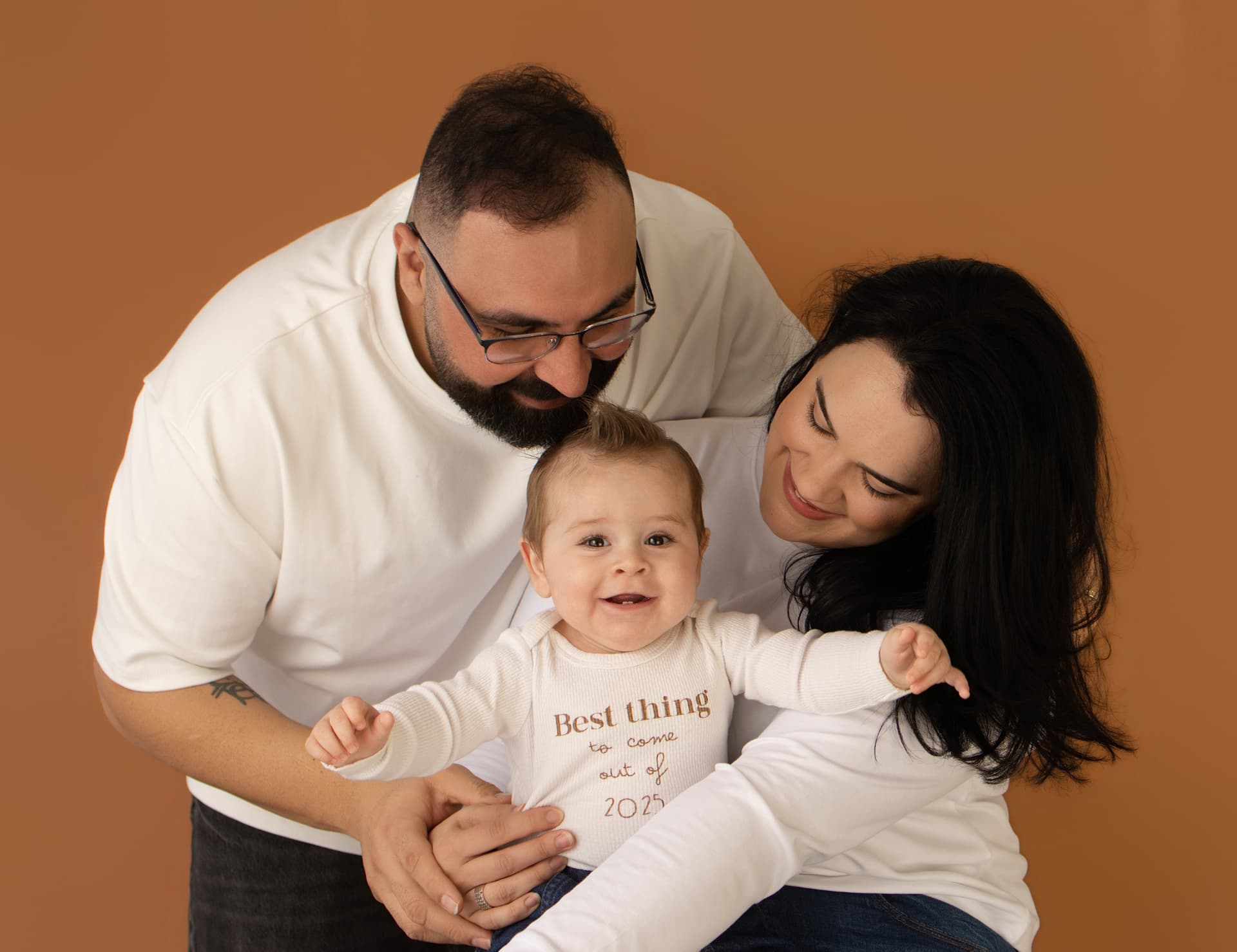 Parents laughing with their smiling baby against a warm terracotta studio backdrop
