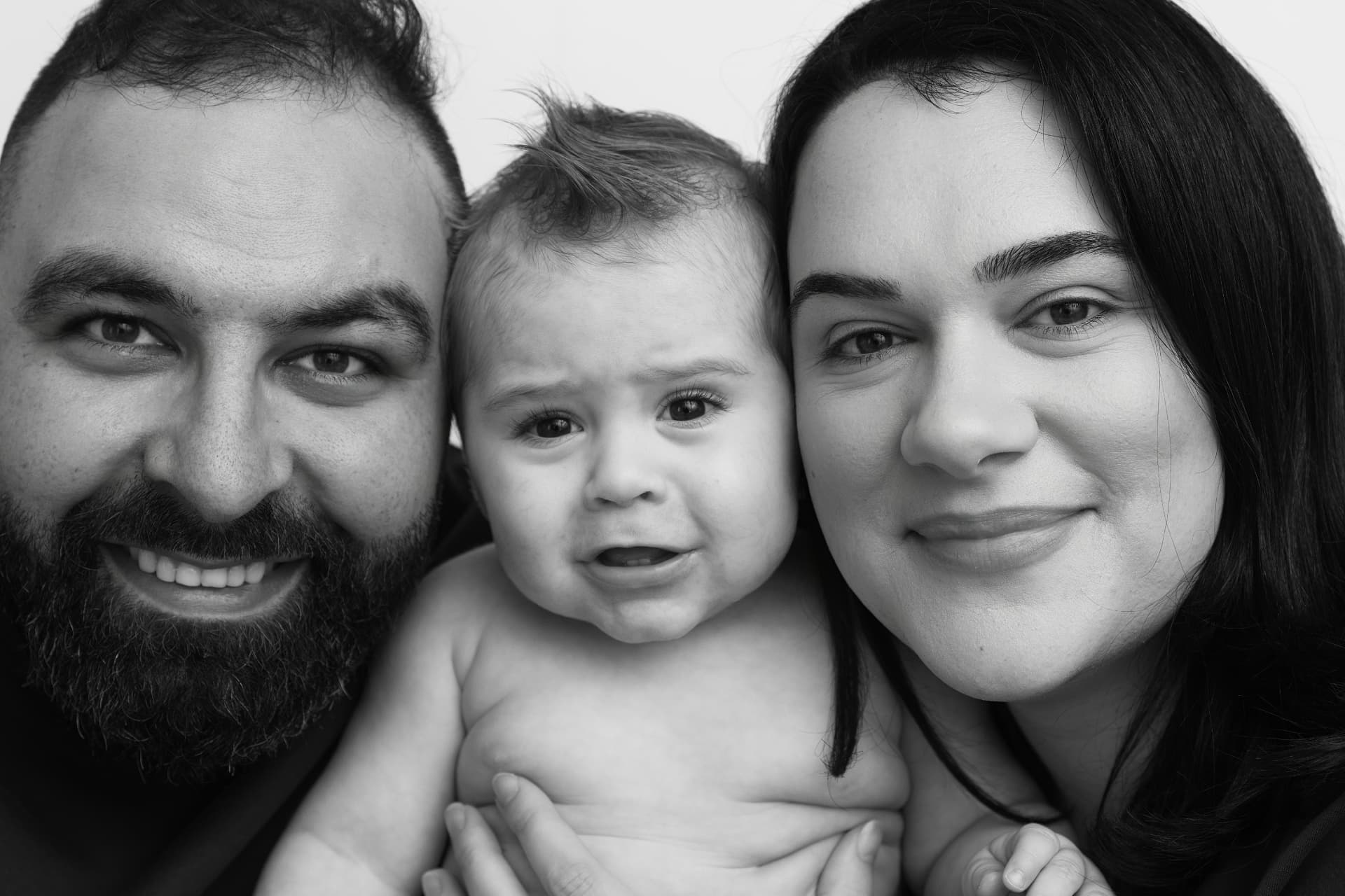 Black and white close-up of parents cheek to cheek with their baby between them