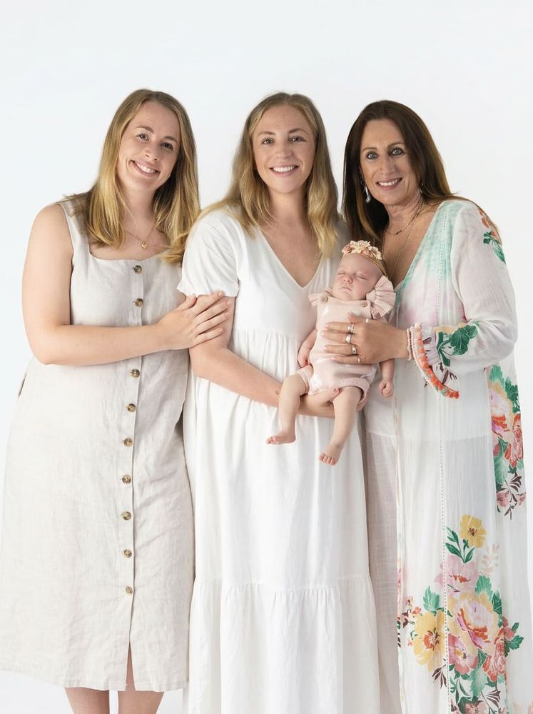 Three generations of women holding newborn baby girl on white studio backdrop