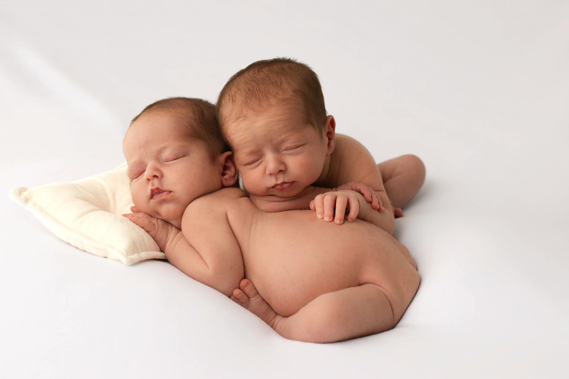 Newborn twins nestled together on a smooth cream backdrop