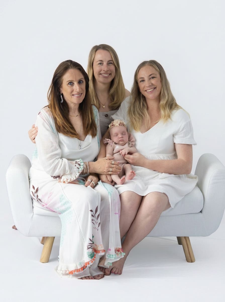 Three generations seated together with newborn on white studio couch