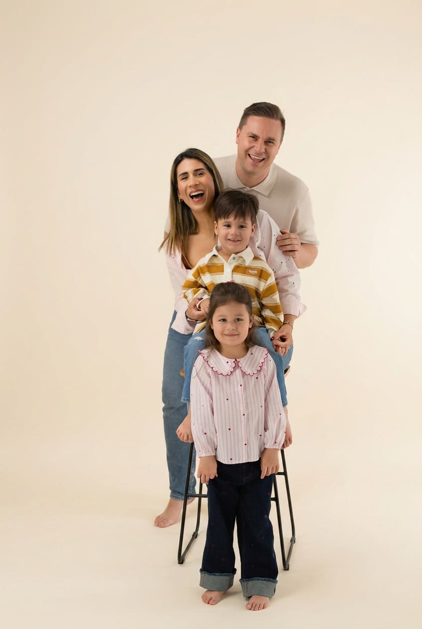 Family of four posed on stools on a soft cream studio backdrop