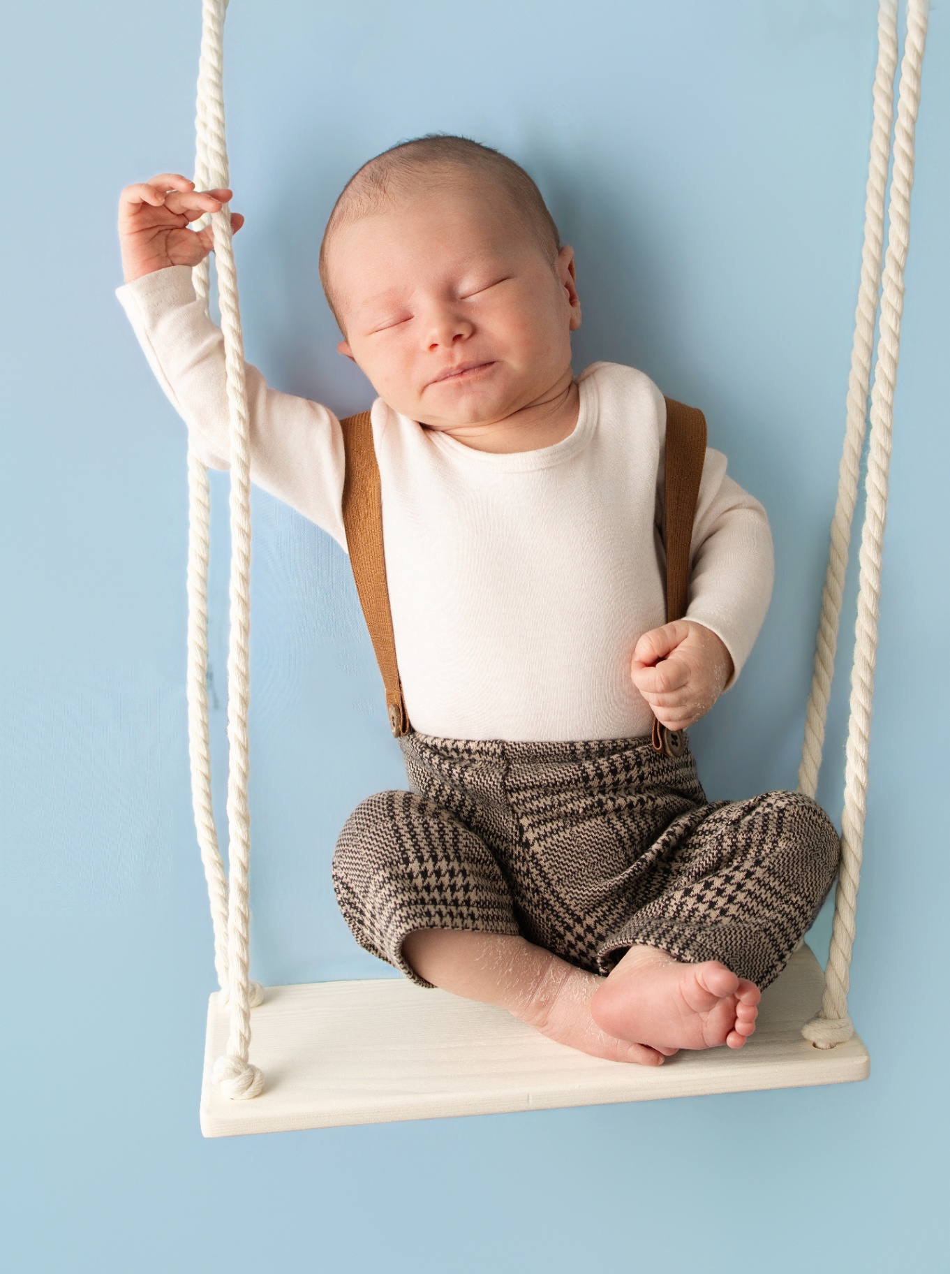 Baby in suspenders seated on a soft studio set