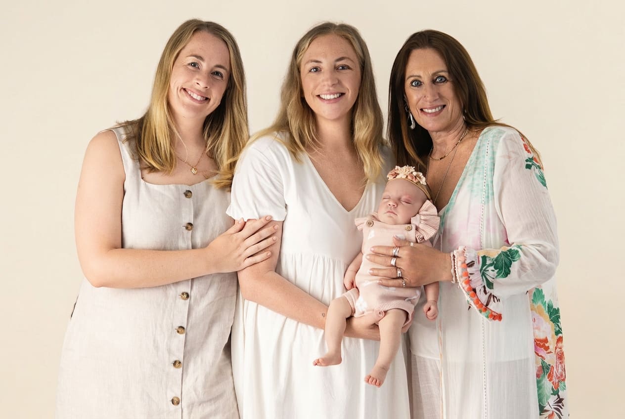 Three generations of women standing with newborn on a soft cream studio backdrop