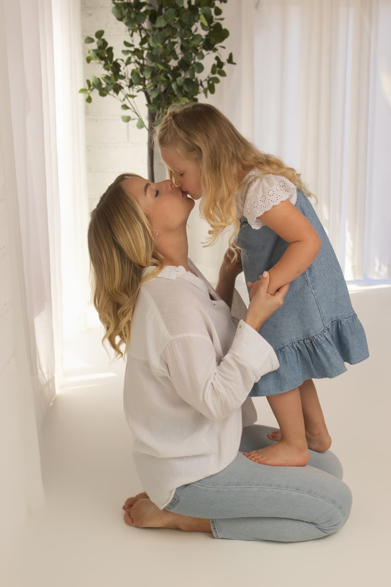 Mother kneeling and kissing her young daughter in soft window light