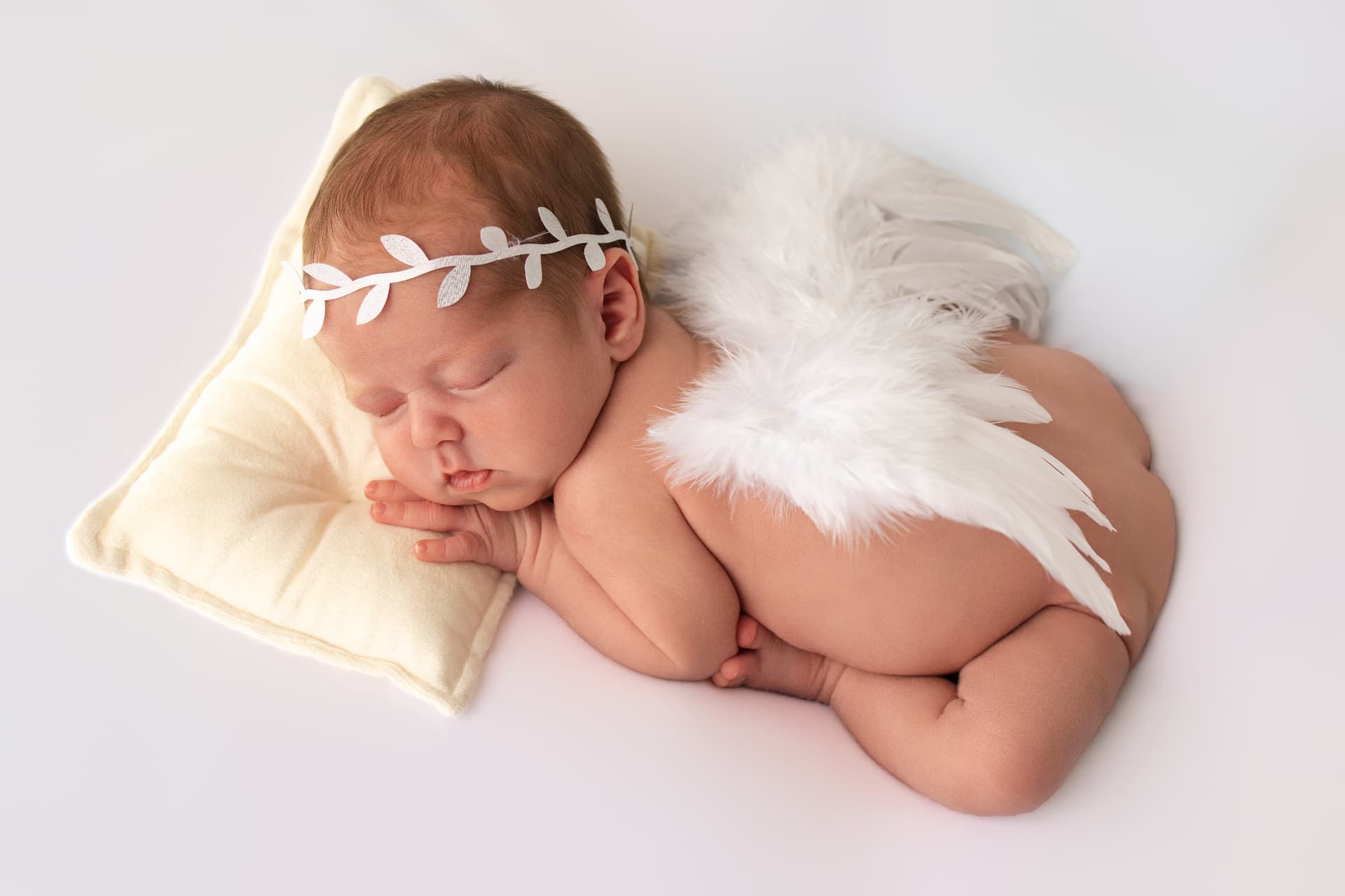 Sleeping newborn resting on a soft cream pillow with delicate feathered angel wings