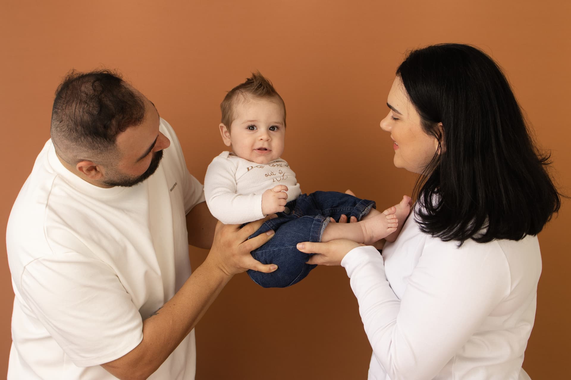 Parents holding their baby up between them on a warm terracotta studio backdrop